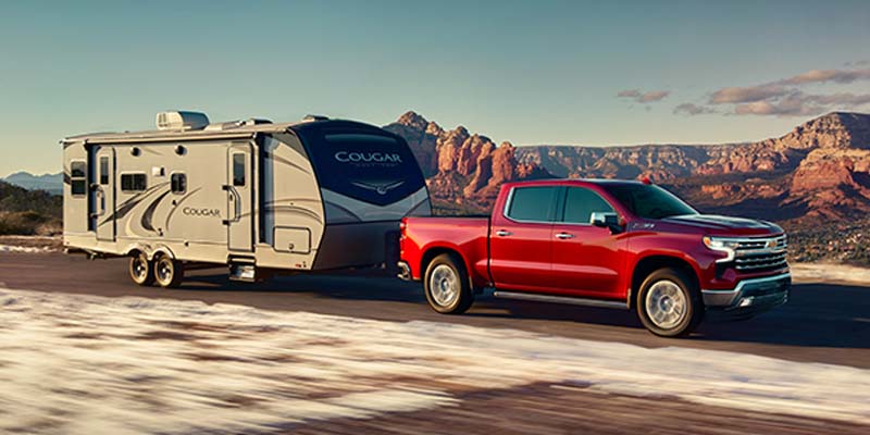 2023 Chevy Silverado 1500 Crew Cab towing a camper trailer on a highway.