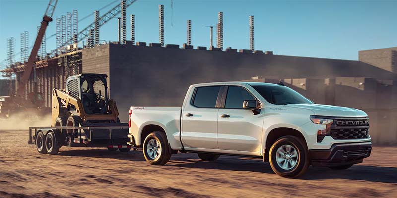2023 Chevrolet Silverado 1500 towing a backhoe from a construction site.